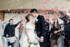 coppia di sposi cinese che si bacia mentre gli ospiti tutti intorno lanciano dei petali di rosa color rosa
